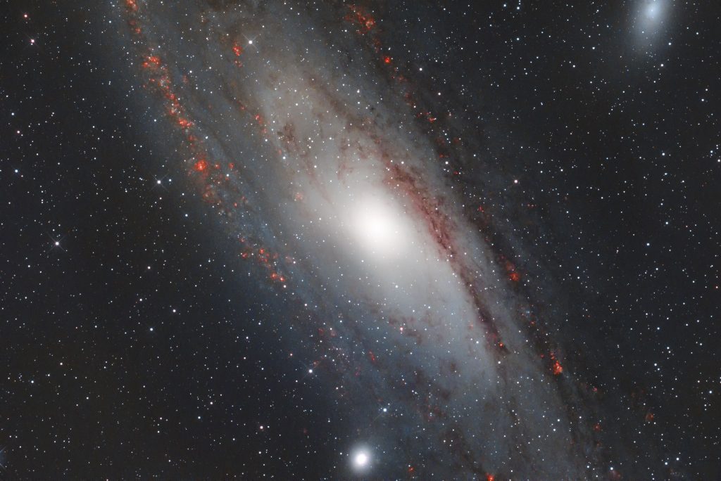 M31. Deutlich treten die roten Wasserstoffwolken (HII-Gebiete) hervor, die sich entlang der Spiralarme verteilen.